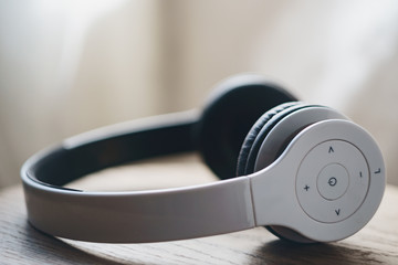 White wireless headphones placed on natural wooden surface on a blurred light curtain background