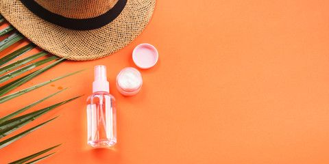 Sun protection concept flat lay with fern, hat, spray bottle and cream. Orange coral background.