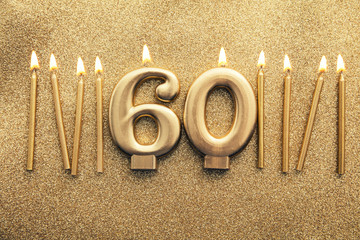 Number 60 gold celebration candle on a glitter background