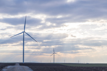 Two wind turbines on agricultural ground with cloudy sky in background