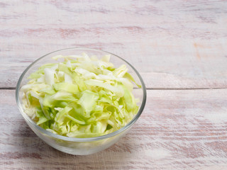 Chopped green cabbage in a transparent bowl, wooden background with copy space
