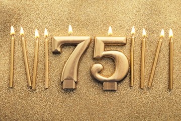 Number 75 gold celebration candle on a glitter background