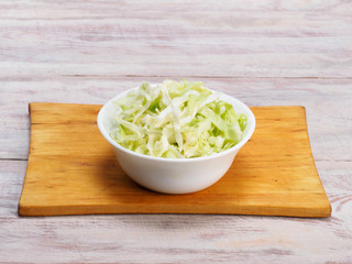 Chopped green cabbage in a white bowl on a cutting board, wooden background with copy space