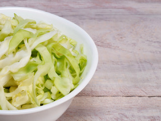 Finely chopped green cabbage in a white bowl on a wooden background with copy space