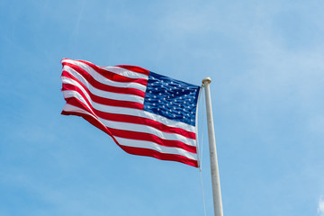 The flag of the United States of America flies in the wind on a flagpole against the blue sky