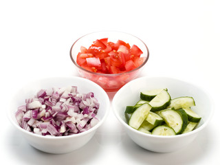 Sliced tomato, red onions and cucumbers in bowls on white background