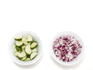 Sliced red onions and cucumbers in a white bowls on white background