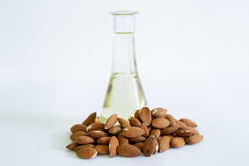Pile of almonds with small bottle with oil in it placed in the middle on a white background – Dry brown seeds with a glass recipient – ingredient used in cosmetics or as an aliment
