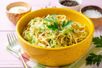 Coleslaw salad with cabbage, carrot and cucumber in bowl on purple wooden background. Selective focus.