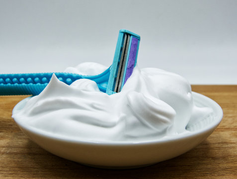 Shaving razor in a bowl filled of shaving foam, wooden table, white background