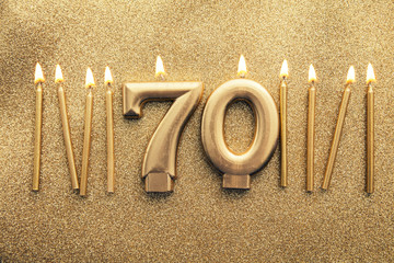 Number 70 gold celebration candle on a glitter background