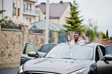 Rich business african woman in silver suv car on sunroof having fun with beer at hand.