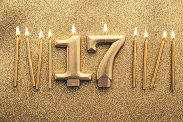 Number 17 gold celebration candle on a glitter background