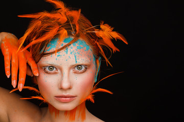 Portrait of a beautiful model with creative make-up and hairstyle using orange feathers