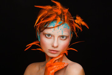 Portrait of a beautiful model with creative make-up and hairstyle using orange feathers