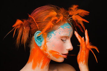 Portrait of a beautiful model with creative make-up and hairstyle using orange feathers