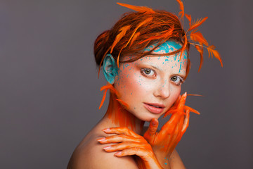 Portrait of a beautiful model with creative make-up and hairstyle using orange feathers