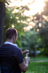 Man holding bottle of water.Sunset in a park with bottled water. Vertical.