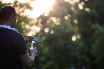 Man holding bottle of water.Sunset in a park with bottled water. Copy space.