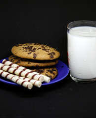 A plate of chocolate chip cookies on a blue plate with a glass of milk on a black background close-up