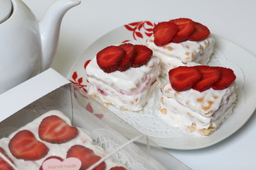 Cake from cookies, sour cream and strawberries. Decorated with strawberry slices. Near the same pastries and teapot.