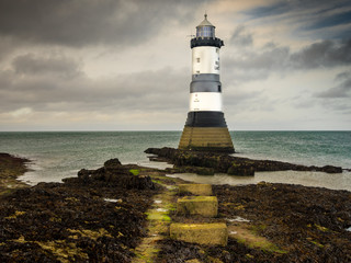 Fototapeta na wymiar Penmon Lighthouse. Penmon Lighthouse is situated on the Angelsey coast. A bell also rings at regular intervals to warn shipping. Cargo ships sail close by.