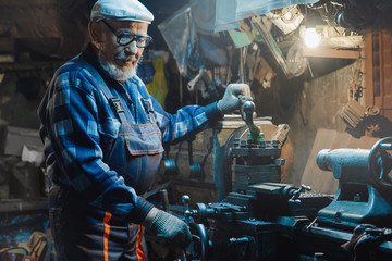 Fototapeta na wymiar Senior elderly male turner handles metal on machine. Concept pension worker industrial, workplace