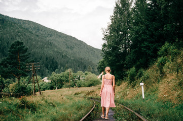 Naklejka premium Young girl walking on the railway. Woman in pink dress walking on railroad tracks.