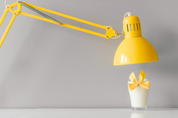 Glass of milk decorated with yellow bowtie standing on table under yellow lamp