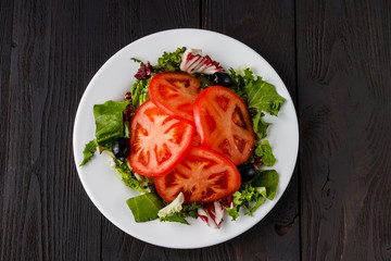 summer salad with tomatoes in white plate on wood table