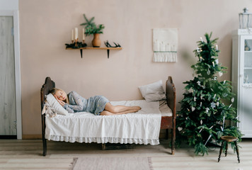 Young beautiful girl sleeping on bed with toy like child in room with christmas tree