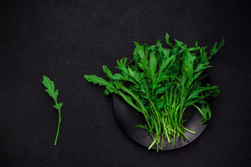 Fresh brunch of arugula on a black plate on a dark background with space for your text. top view