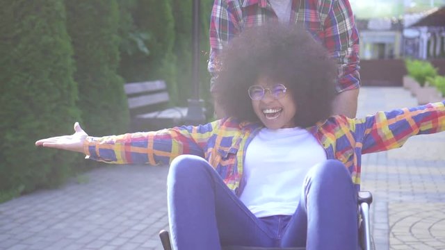 portrait of a positive smiling young African American woman disabled in a wheelchair and her friend rejoices and raises her hands close-up