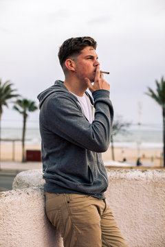 Young man smoking a joint with palm trees in the background