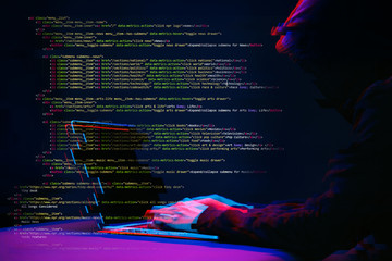 Hacker working with laptop in dark room with digital interface around. Image with glitch effect.