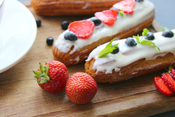 Delicious eclairs with strawberries and blueberries on a wooden cutting Board. Copy space. Beautiful and delicious dessert.