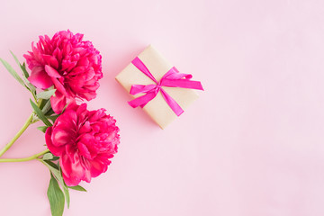 Flat lay composition with red peonies and gift box on a pink background