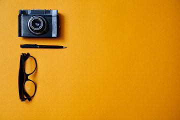 Blogging, blog and blogger or social media concept: glasses, photo camera and a pen on the yellow background. Flat lay