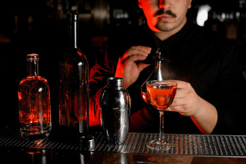 Close-up of bottles, shaker, cocktail and bartender with sprayer