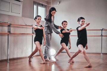 Obraz premium Three young diligent girls have a ballet training with their attractive teacher at bright training room.