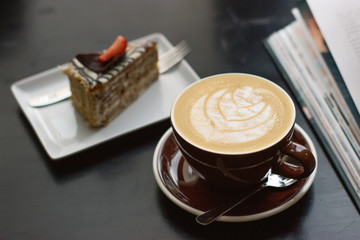 A Cup of coffee with latte art with a delicious piece of cake. Beautiful foam, brown ceramic Cup, space for design and text.