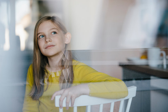 Portrait of a girl sitting on chair at home looking up