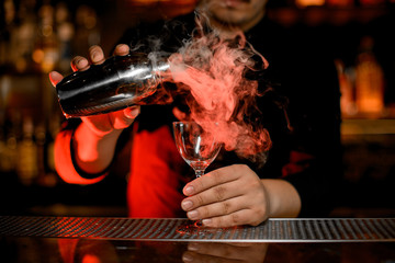 Bartender pouring steamy cocktail from shaker to glass