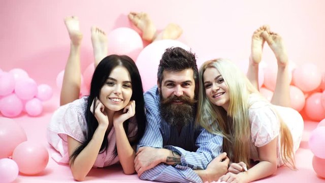 Cheerful morning concept. Man and women, friends on smiling faces lay pink background. Lovers in love happy together. Bearded man and women in domestic clothes, pajamas. Threesome relaxing in morning.