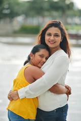 Obraz premium Portrait of happy Indian mother standing and embracing her daughter while they standing outdoors and smiling at camera