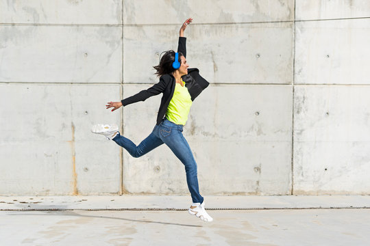 Woman with blue headphones listening music, jumping in the air