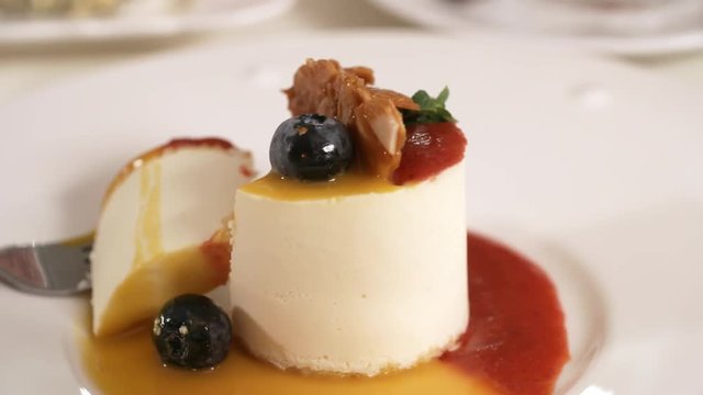 Close-up object shot of tasty cheesecake with blueberries and fruit coulis sitting on table in restaurant, with one piece sliced off with fork, and left on plate
