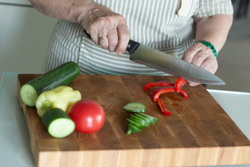 Senior or older woman cooking salad in kitchen. Healthy food concept. Healthy lifestyle. Grandma prepares a healthy meal for her grandchildren.