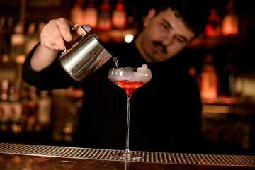 Bartender pours cocktail from a steel mug