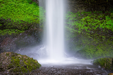 Fototapeta premium A beautiful waterfall splashing into a pool beneath rocks covered in lush green moss and vegetation - Latourell Falls in Oregon's Columbia River Gorge